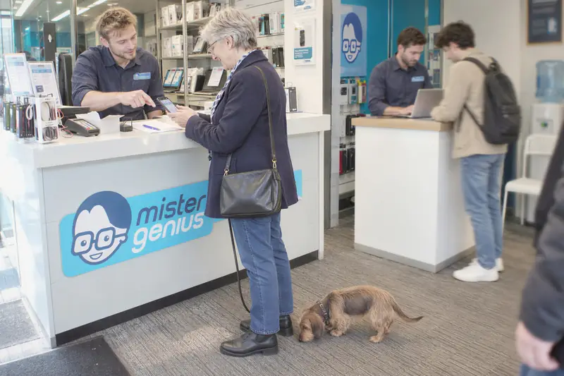 Technicien Mister Genius rendant un smartphone réparé à une cliente accompagnée de son chien
