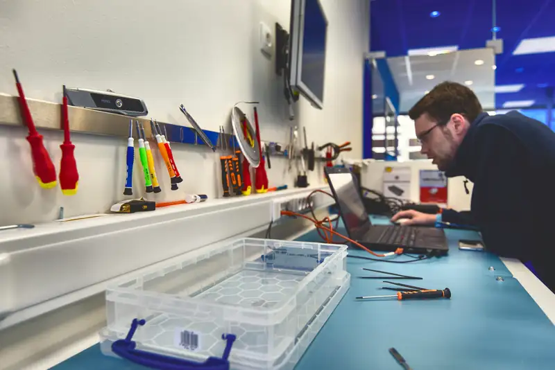 Technician at workbench, tools on wall, Mister Genius store Wavre